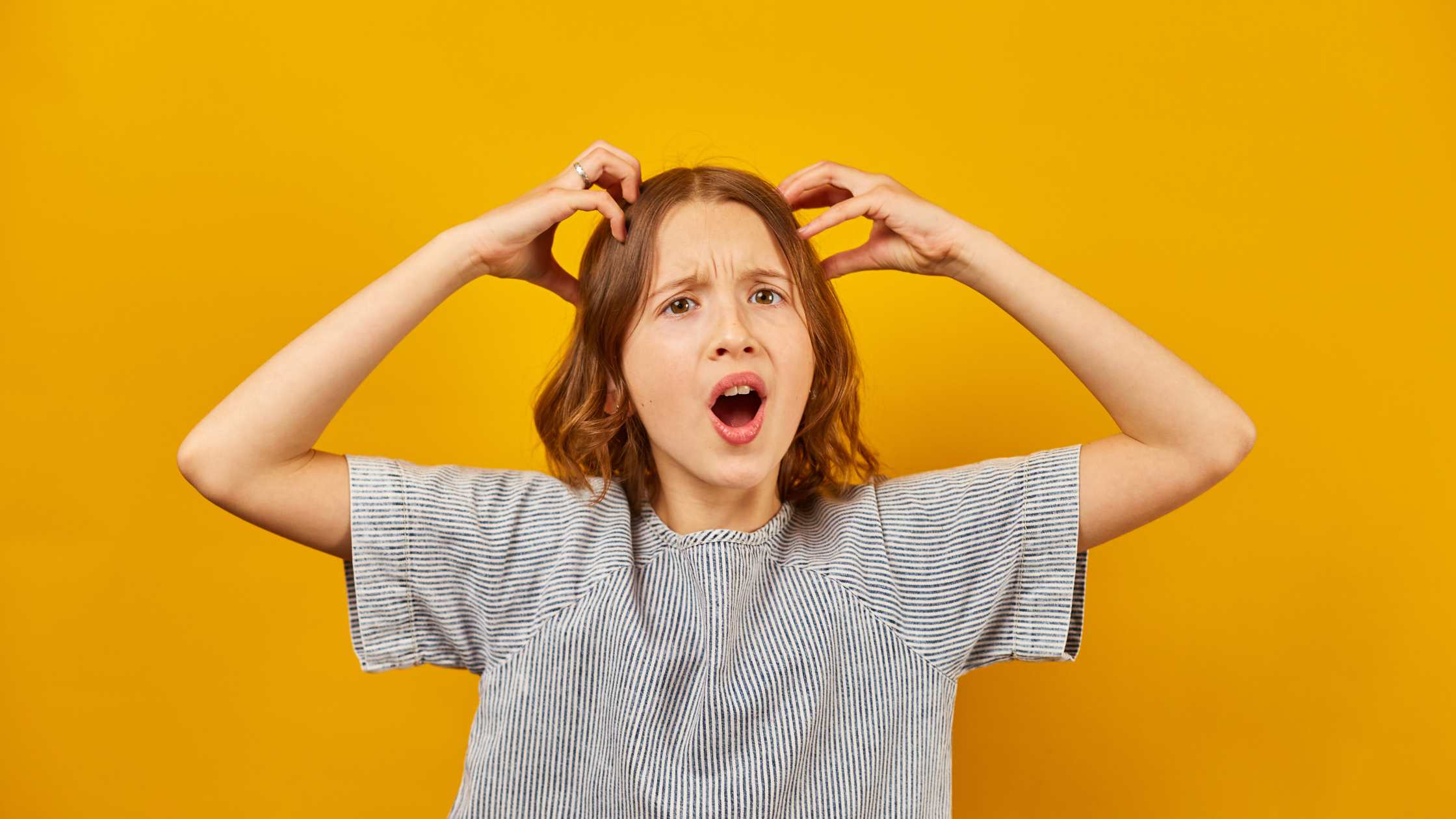 Teen expressing frustration with hands on head against a yellow background, illustrating common behavioral signs of emotional dysregulation in teens.