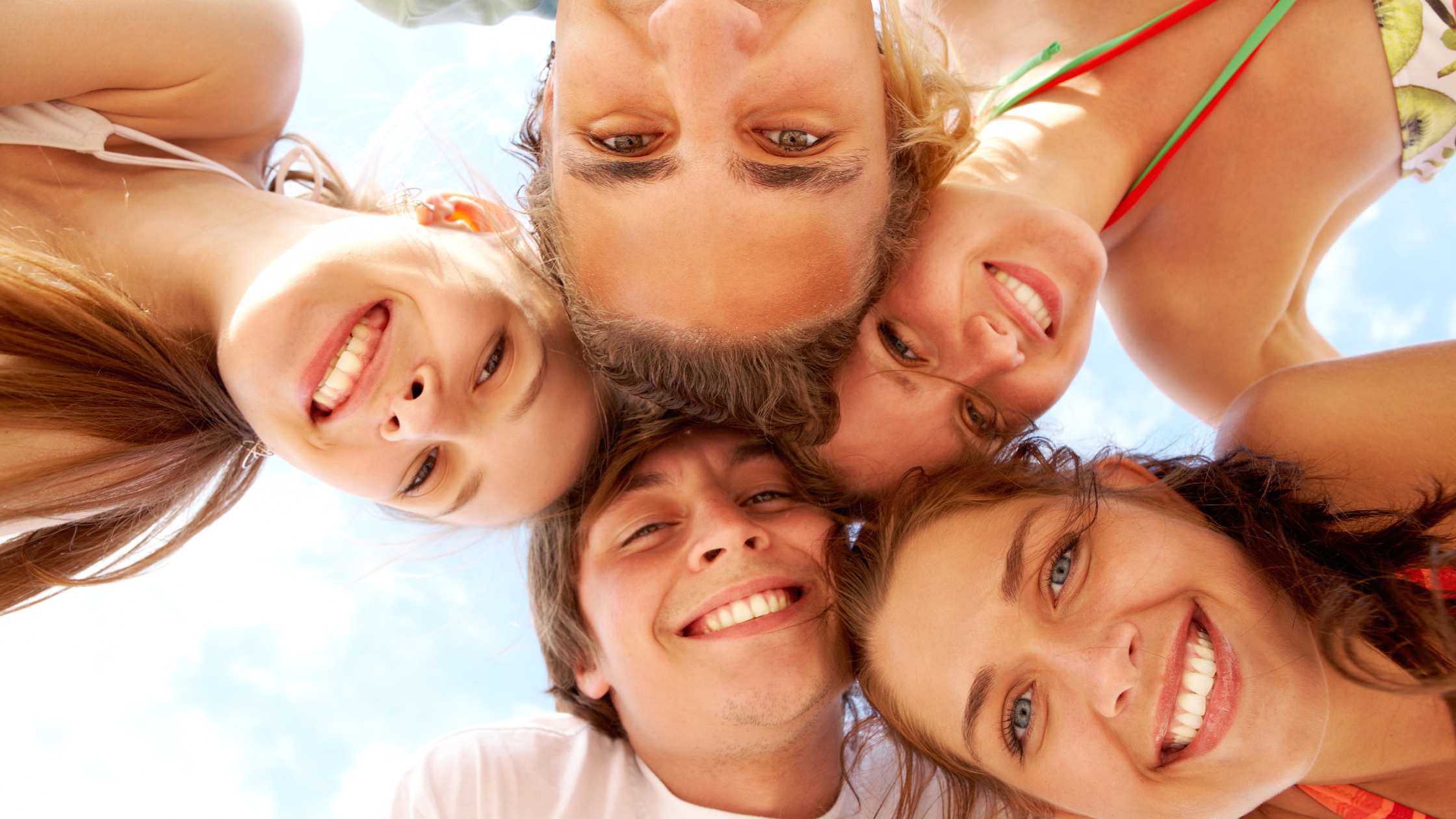 Group of happy teens smiling in a huddle under the sky, symbolizing positive outcomes of emotional dysregulation treatment at Nexus Teen Academy.