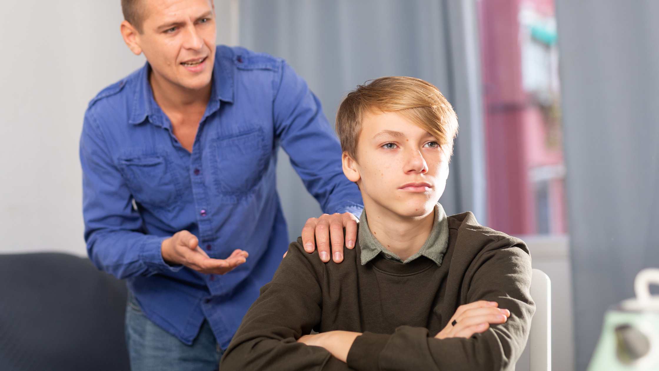 Teen with arms crossed, looking away while an adult tries to talk, symbolizing the long-term consequences of ignoring emotional dysregulation in teens.