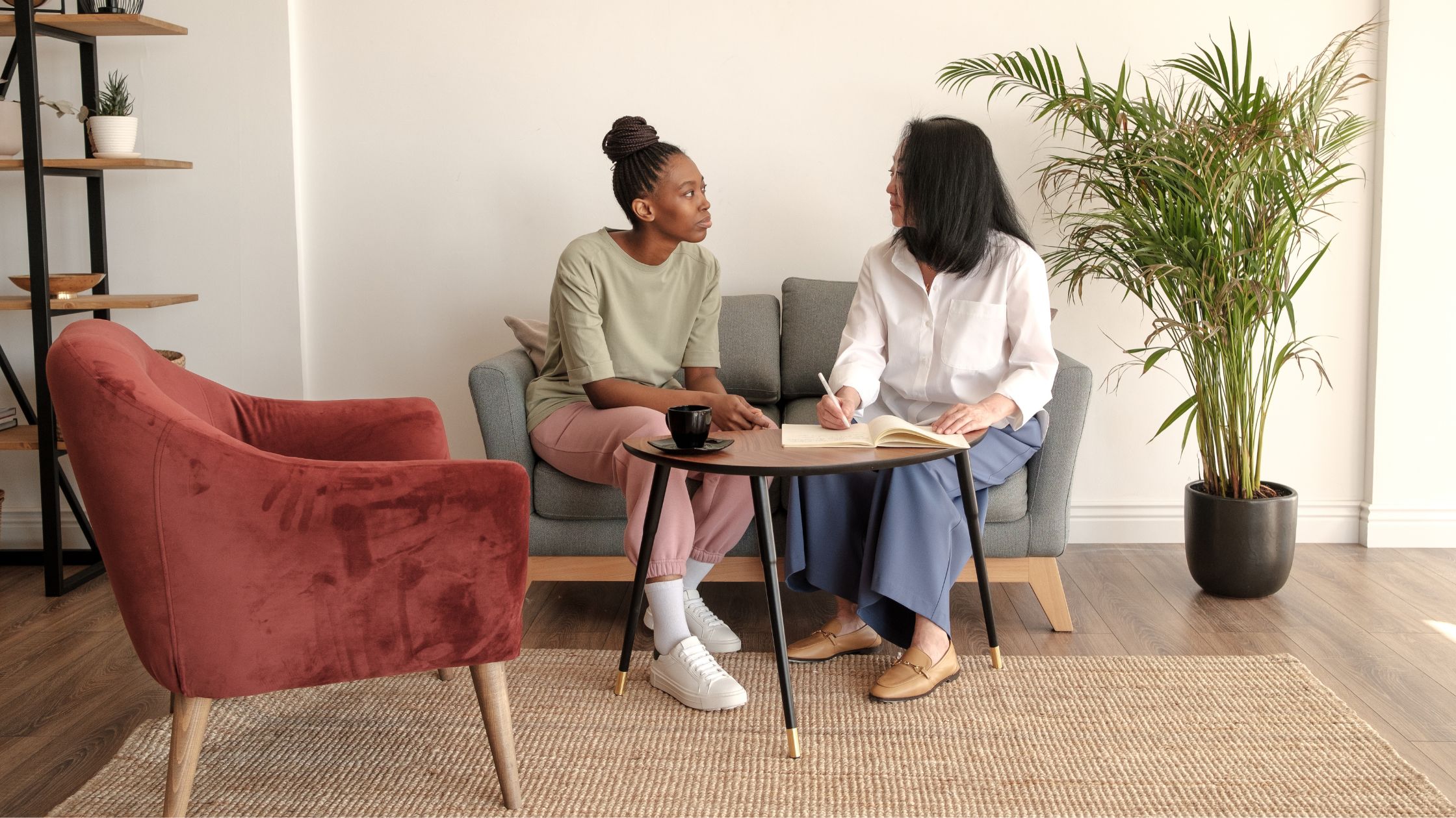 Therapist and teen sitting in a cozy room, engaged in a thoughtful conversation, with a notebook and coffee, promoting open communication in art therapy.