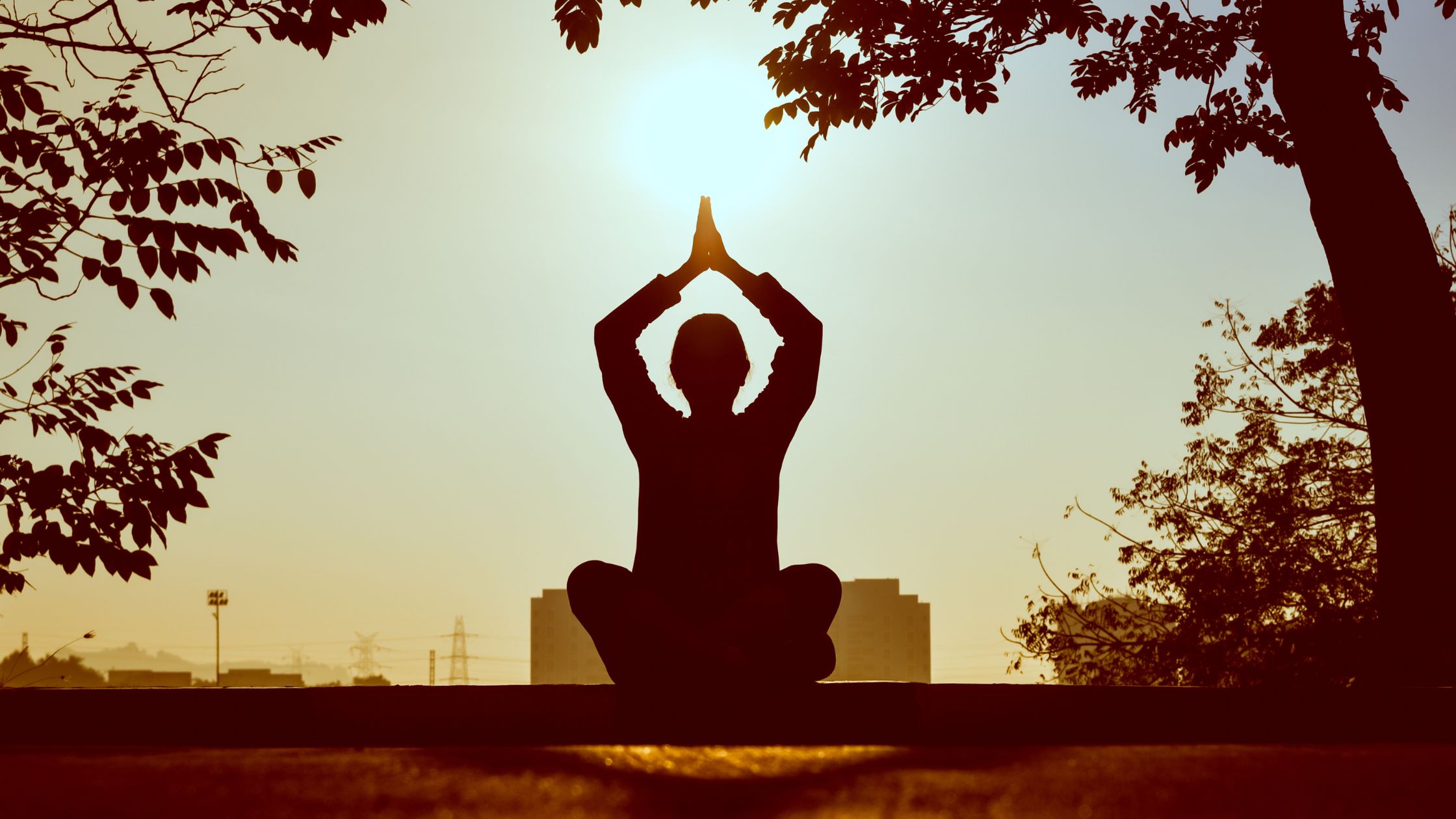 Silhouette of a person meditating outdoors at sunrise, sitting cross-legged with hands in a prayer position, symbolizing peace and mindfulness. Key benefits of meditation for teens.