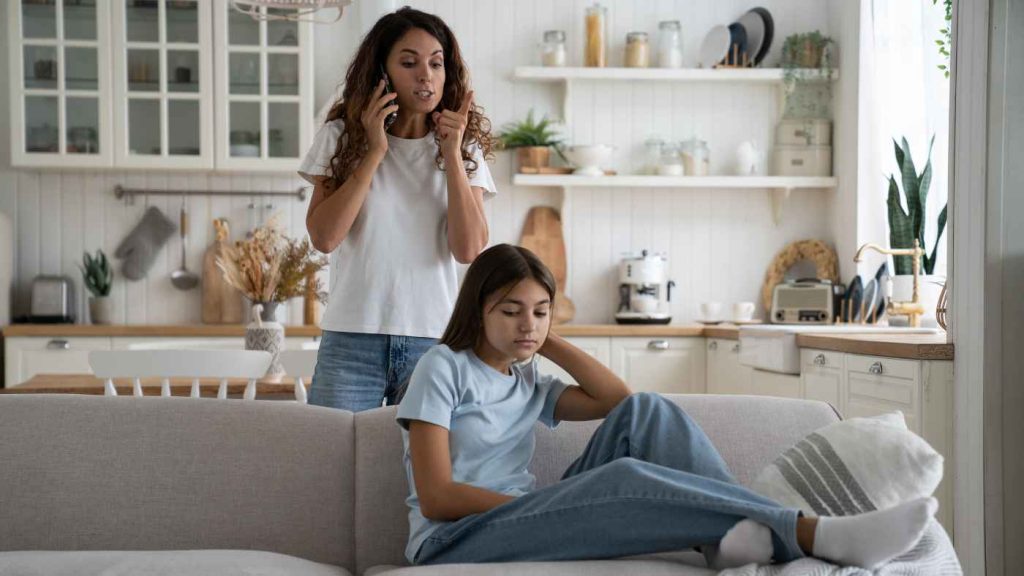 Mother on phone appearing concerned while teen girl looks withdrawn, illustrating stress before inpatient mood disorder treatment.