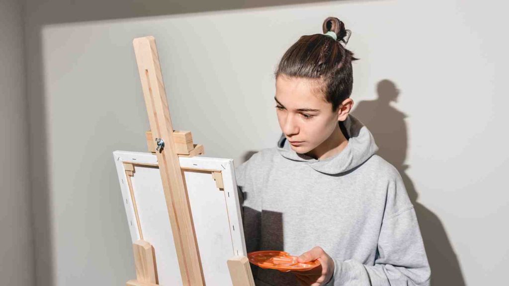 Teen focused on painting at an easel, illustrating art therapy as part of a holistic approach to mental health treatment.