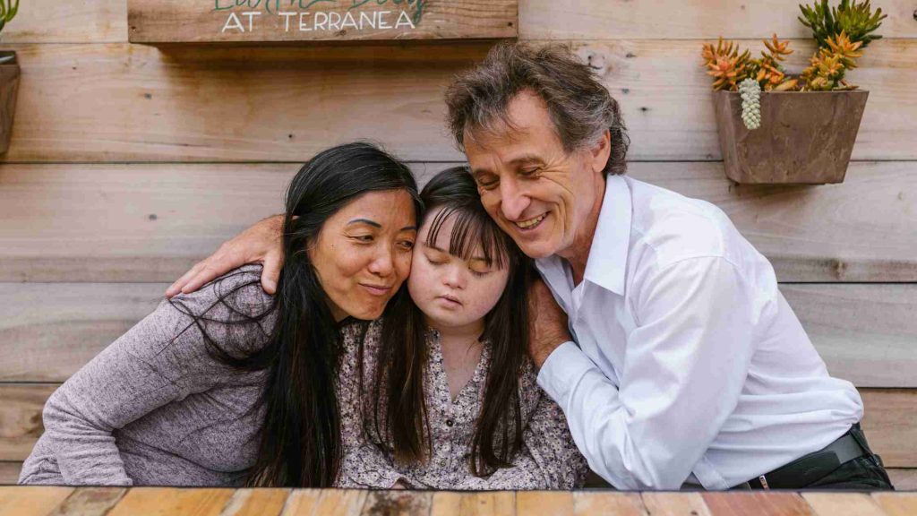 Parents smiling and embracing their teen in a warm family hug, showing acceptance and support.