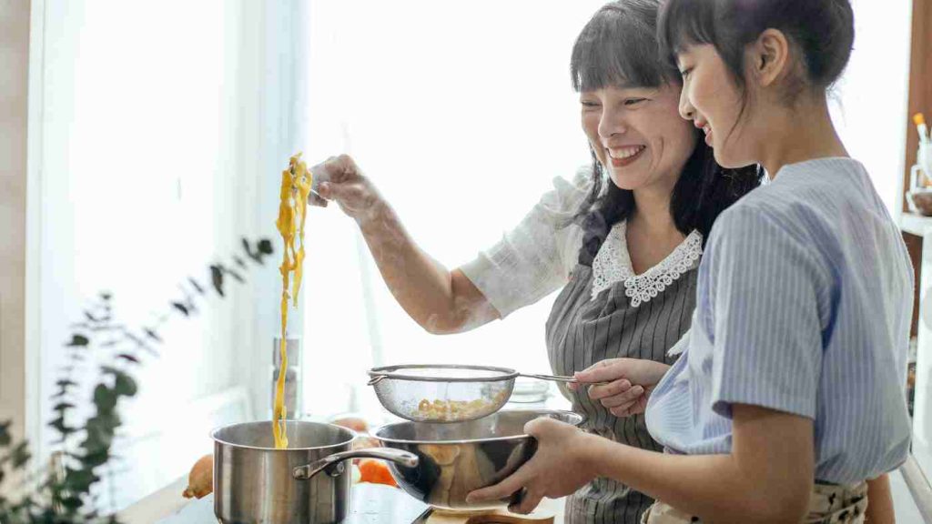 Parent and child cooking vegetables together, caregiver guiding teen’s healthy eating habits in a home kitchen setting.