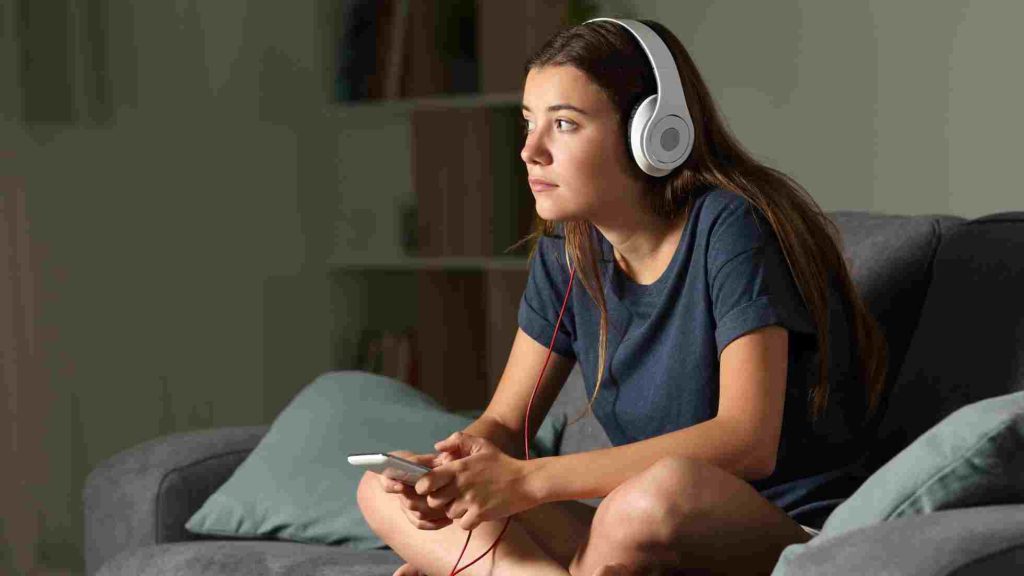 Teen wearing headphones on a couch, holding a device calmly as she practices mindfulness and deep breathing.