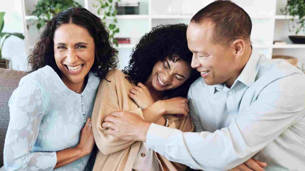 Two parents and their teen share a warm, supportive embrace on the sofa, smiling as they connect.