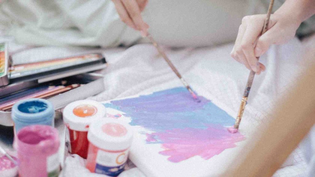 Two teens paint with brushes and vibrant colors, reflecting self-expression and emotional healing through art therapy.