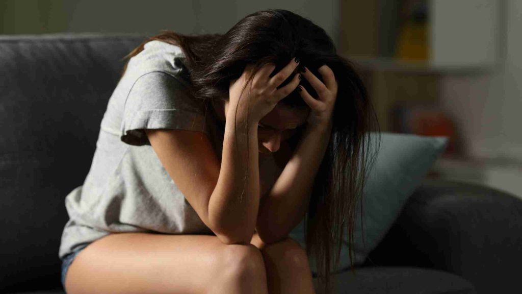 Teen hunched on couch, hands gripping head, illustrating distress when mental illness goes unaddressed.