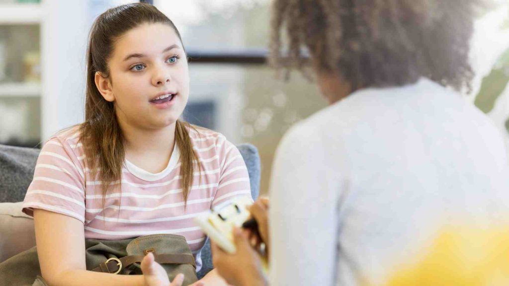 Teen speaking with a counselor across a table, sharing concerns in a supportive therapy setting.