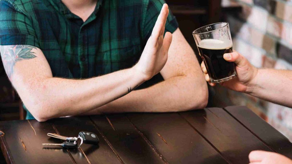 Hands refusing a beer glass beside car keys on a table, highlighting substance use and physical health factors in teen depression.