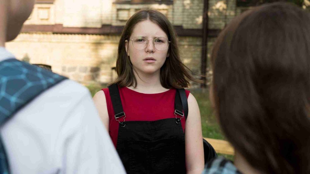 Teen girl outdoors facing peers, looking confused and anxious, depicting internal emotional struggles and psychological causes.