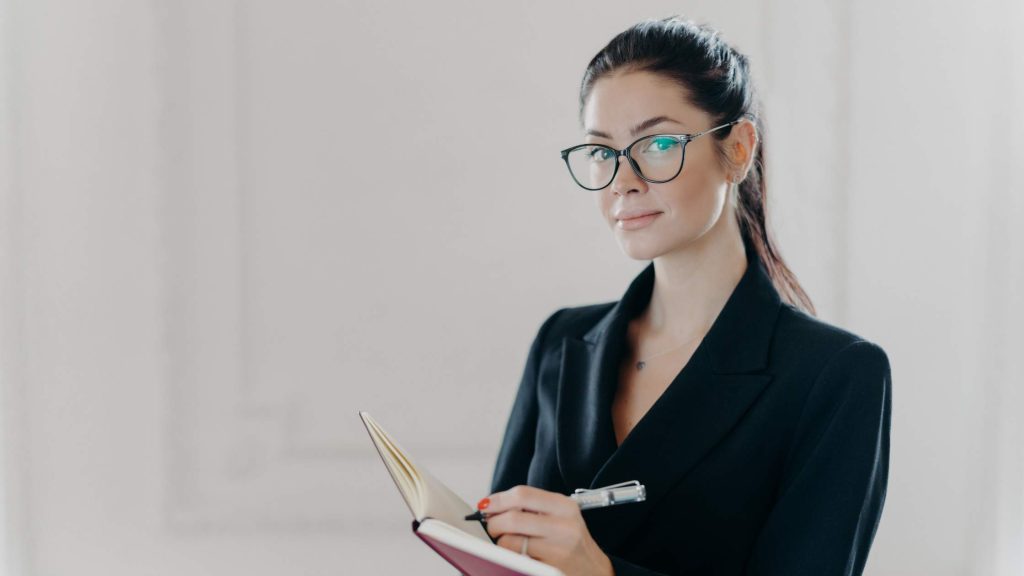 Confident female professional in glasses holding a notebook and pen, representing experts qualified to diagnose ADHD in teens.