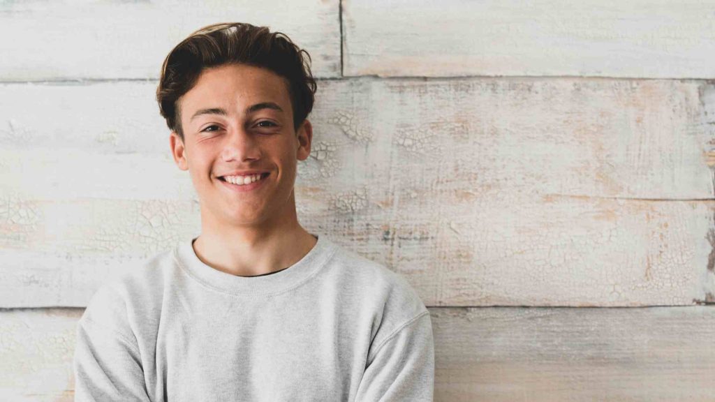 Smiling teenage boy standing confidently, representing the supportive and positive environment provided by boys’ homes.
