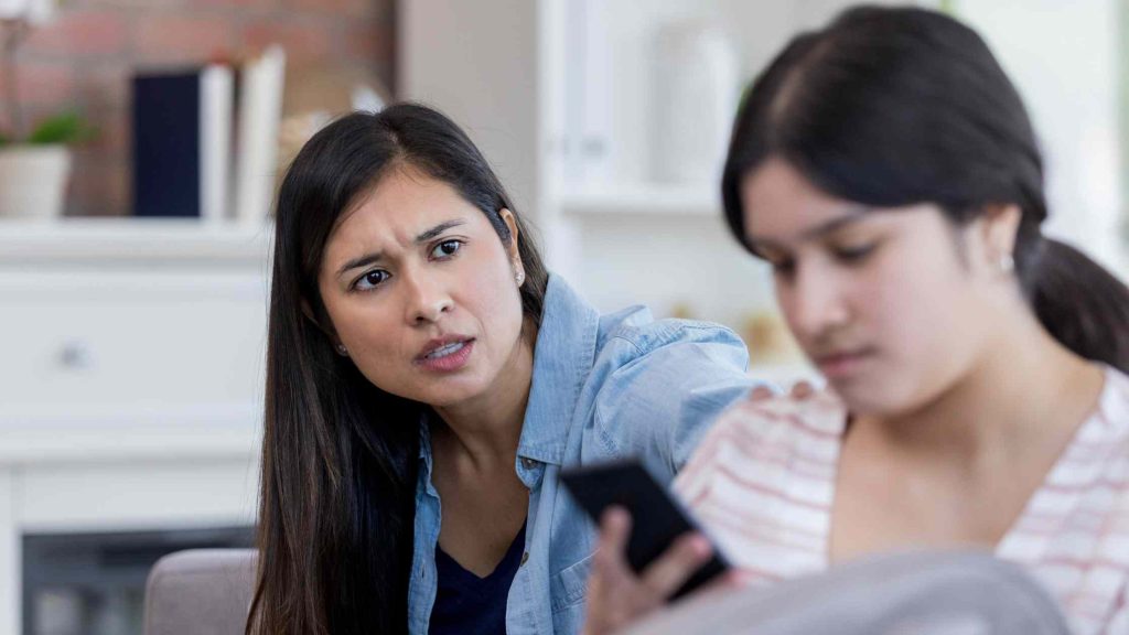 Concerned mother talking to her teenage daughter who ignores her while using a phone, showing teen disobedience to parents.