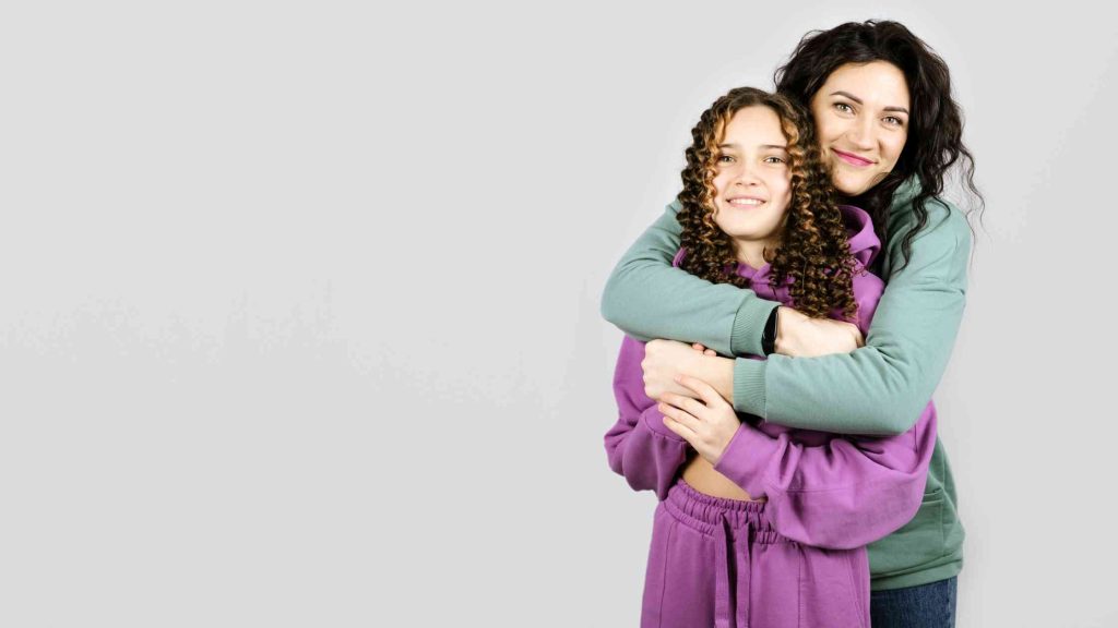 A caring adult hugs a smiling teen, symbolizing emotional safety, trust, and healing goals achieved through trauma therapy.