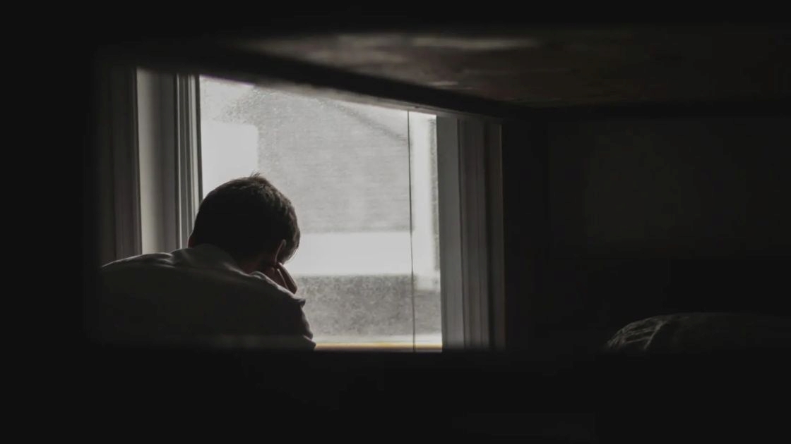 Teen sitting alone in a dark room by the window, showing isolation, emotional numbness, and deep hopelessness.