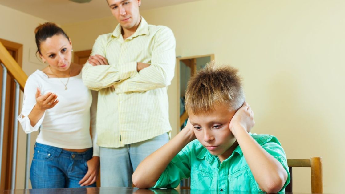 Parents confronting upset boy at table, reflecting boundary setting challenges and rule resistance at home.