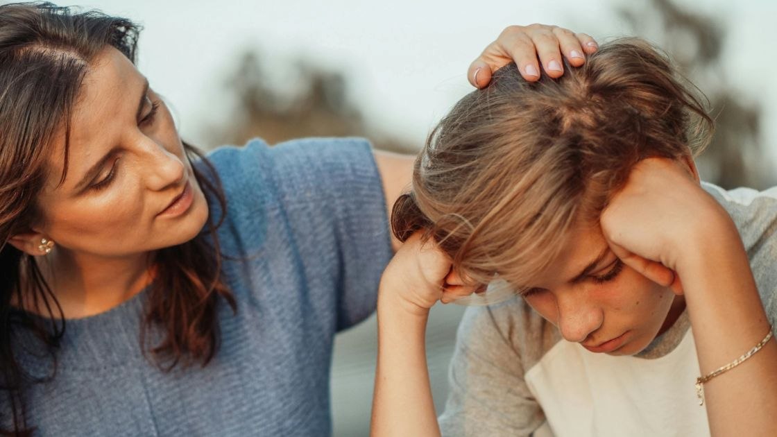 Mother gently comforting her teen son during a serious talk about teen bullying and emotional distress.