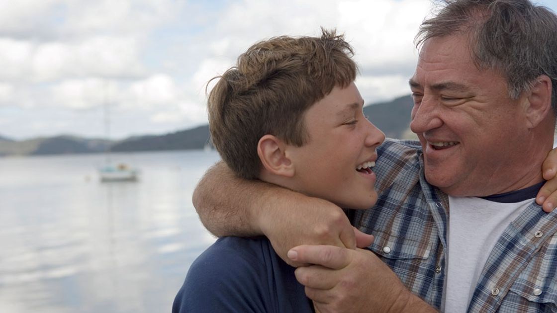 Father embracing smiling teenage son outdoors, symbolizing trust, emotional repair, and connection after conflict.