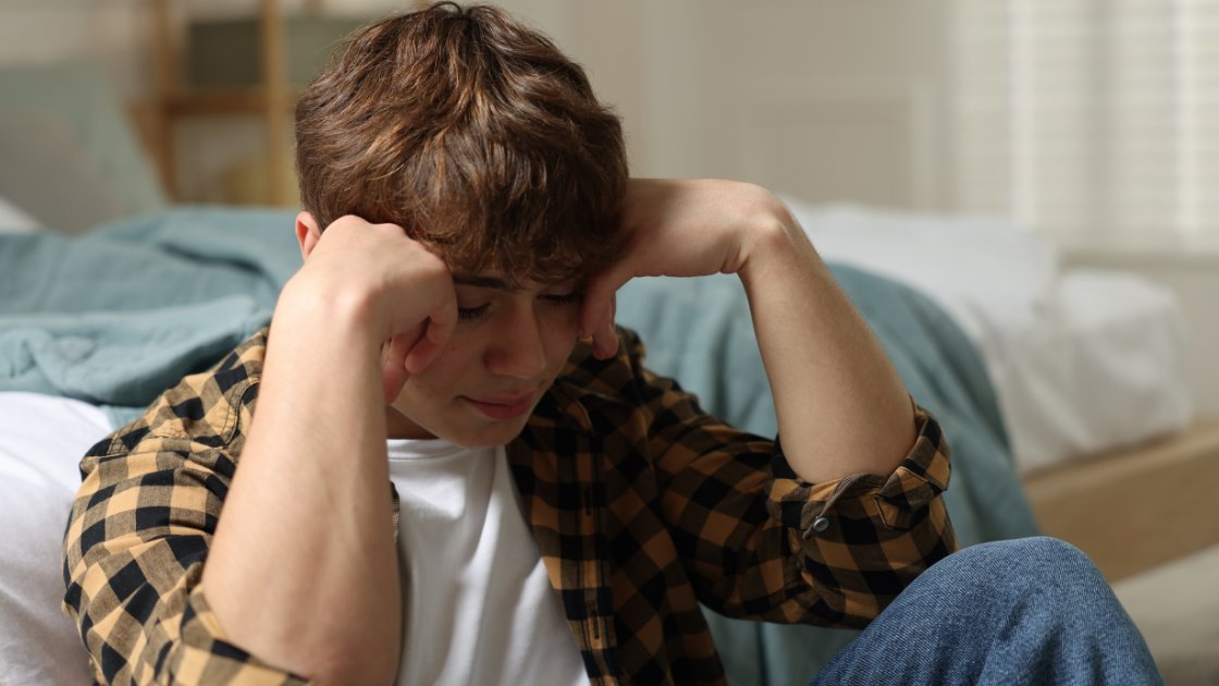 Teen boy sitting distressed with head in hands; shows emotional and behavioral signs parents may notice with party drug use.