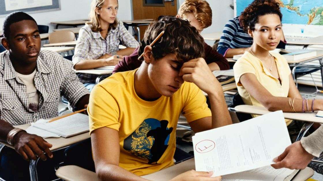 Teen boy in a classroom holding failed test, showing stress that may signal deeper mental health struggles.