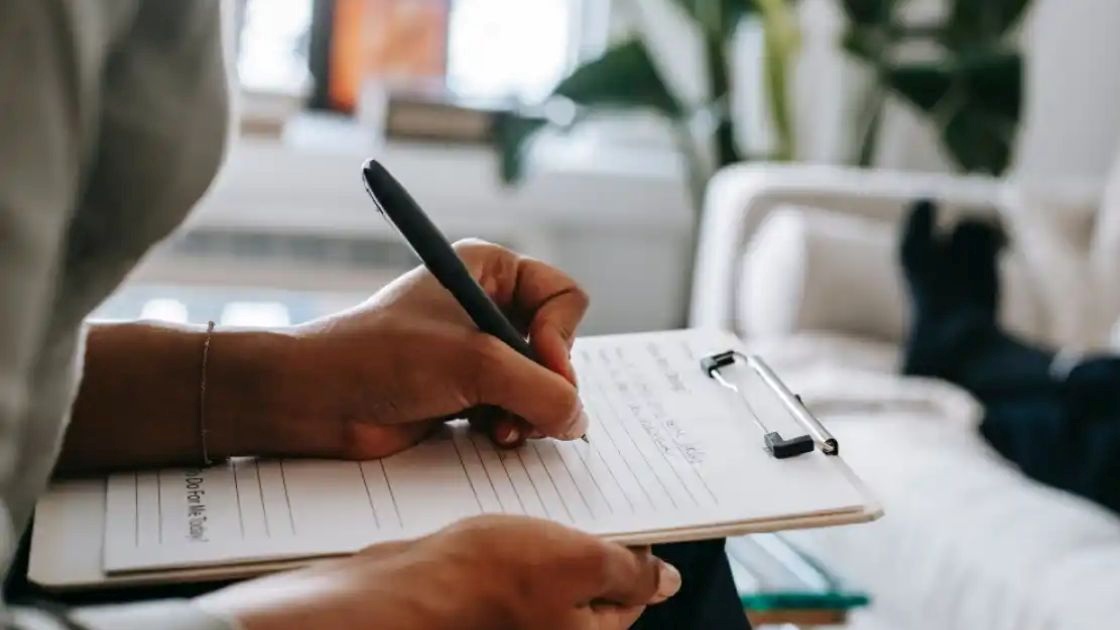 Teen in therapy session listening cautiously as counselor takes notes, reflecting hesitation and lack of connection.
