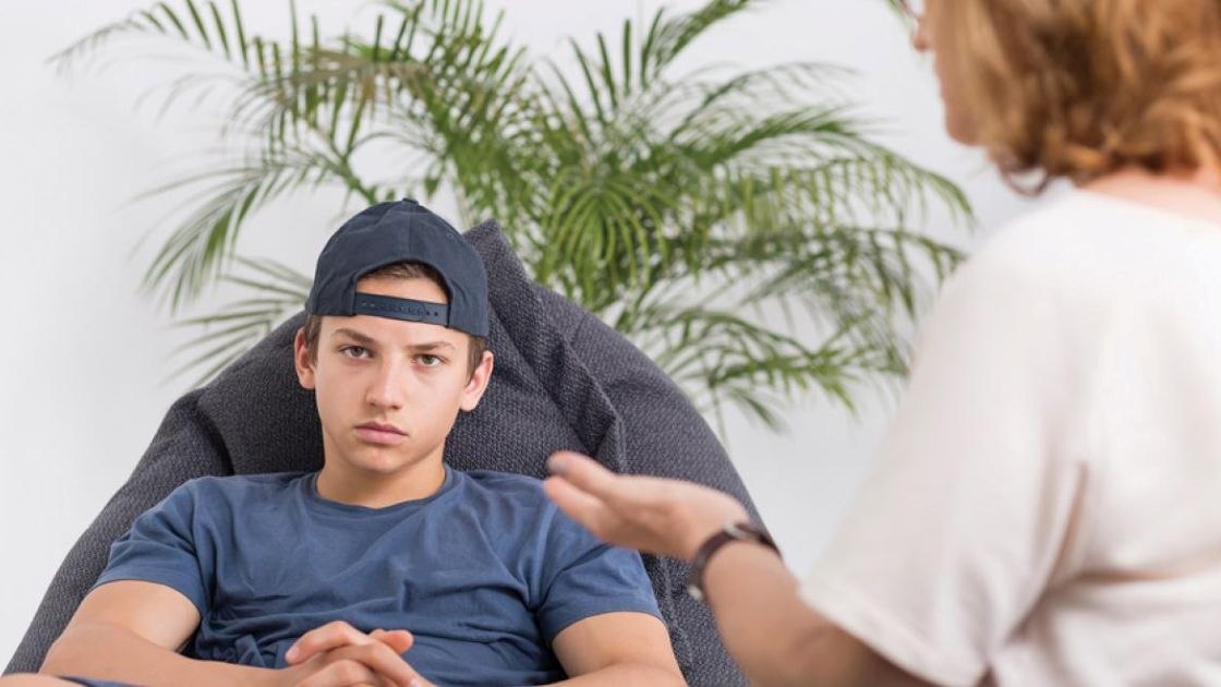 Teen boy sitting defiantly as parent gestures, illustrating how yelling and punishment escalate conflict and defiance.