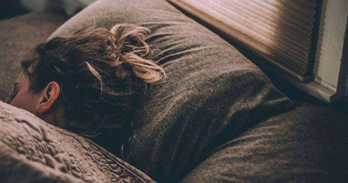 Teen sleeping in bed, representing the need for calm, supportive steps when parents can't get kid out of bed each morning.
