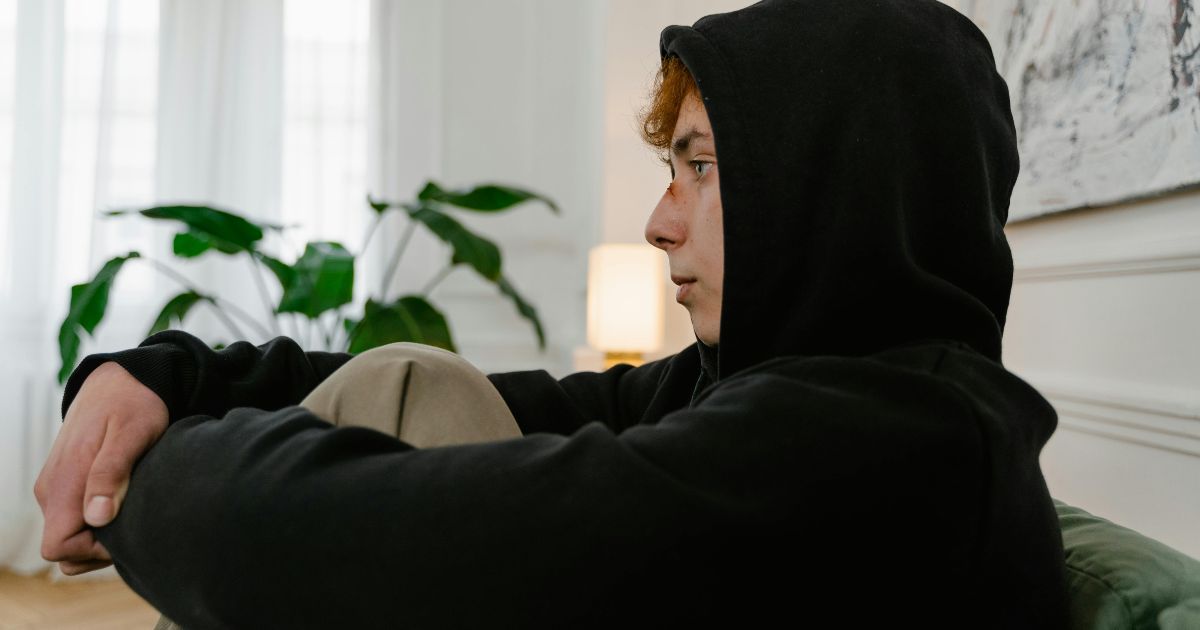 Teenage boy in a hoodie sitting alone at home, withdrawn and irritable
